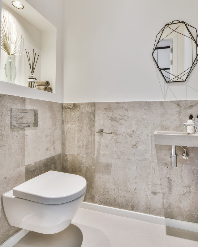 A compact yet opulent bathroom in Hoboken, NJ, featuring a modern hanging toilet and large tan marble wall tiles, exuding an aura of spaciousness and regal elegance, a harmonious blend of form and function by Hoboken Bathroom Renovation.